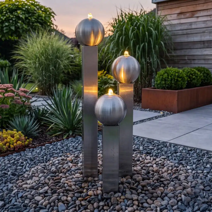 Hoher Edelstahlbrunnen Balance Sphera 145 cm mit stimmungsvoller LED-Beleuchtung im abendlichen, modernen Garten
