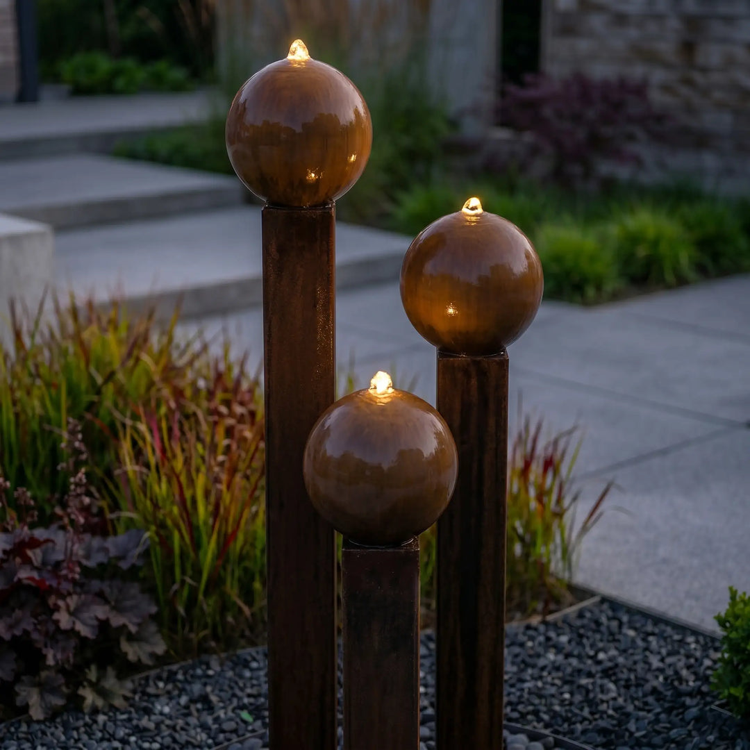 Balance Sphera Cortenstahl-Gartenbrunnen mit warmweißer LED-Beleuchtung oberhalb der Kugeln bei Abenddämmerung