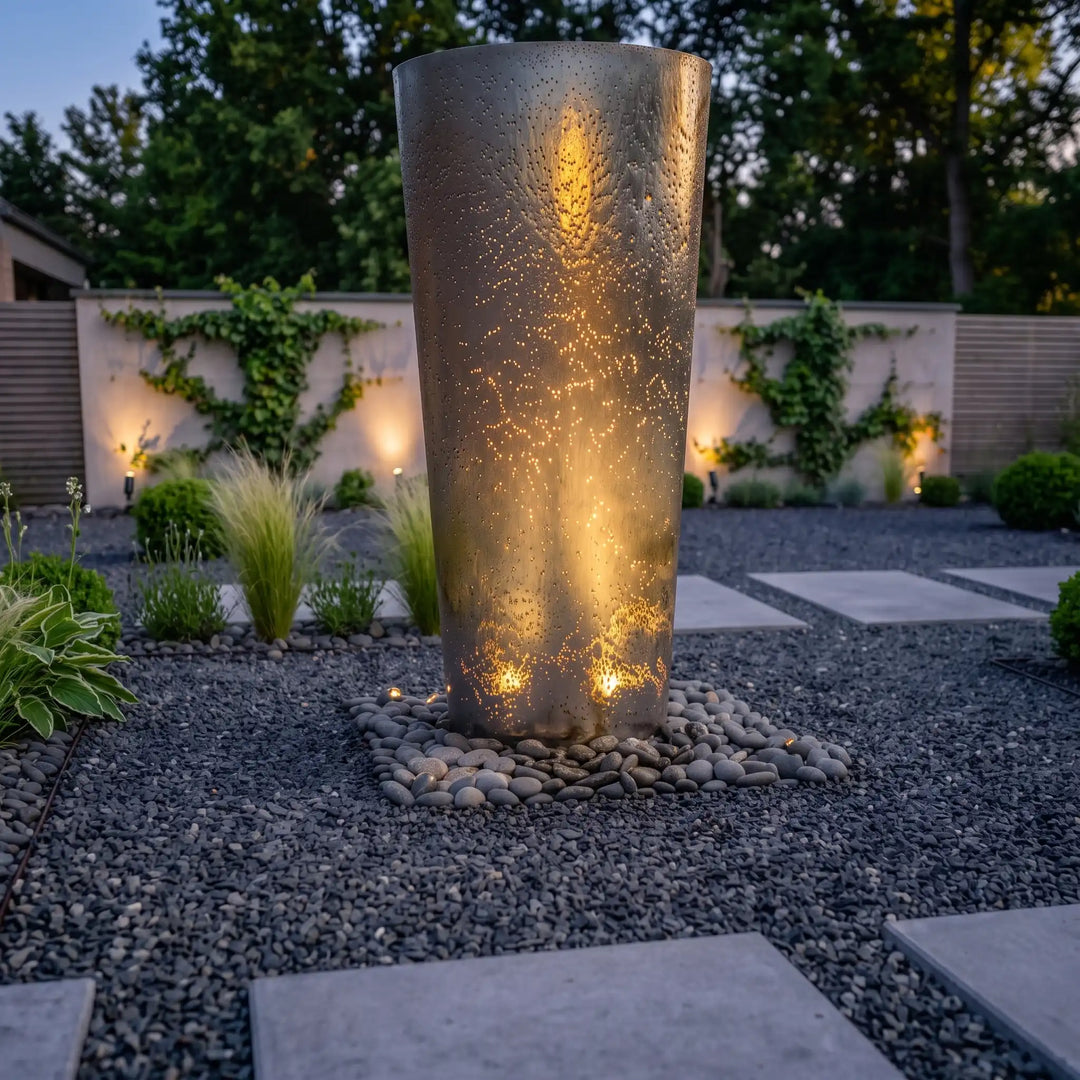 Ellipse Edelstahl-Gartenbrunnen mit externem Erdspießstrahler am Abend
