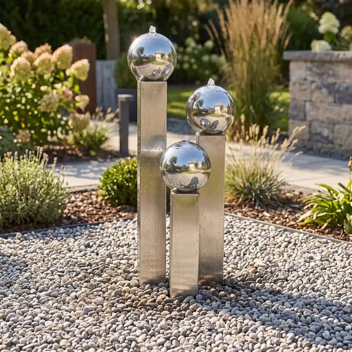 Kompakter Edelstahl-Gartenbrunnen Balance Sphera mit drei Kugeln neben einer Terrasse