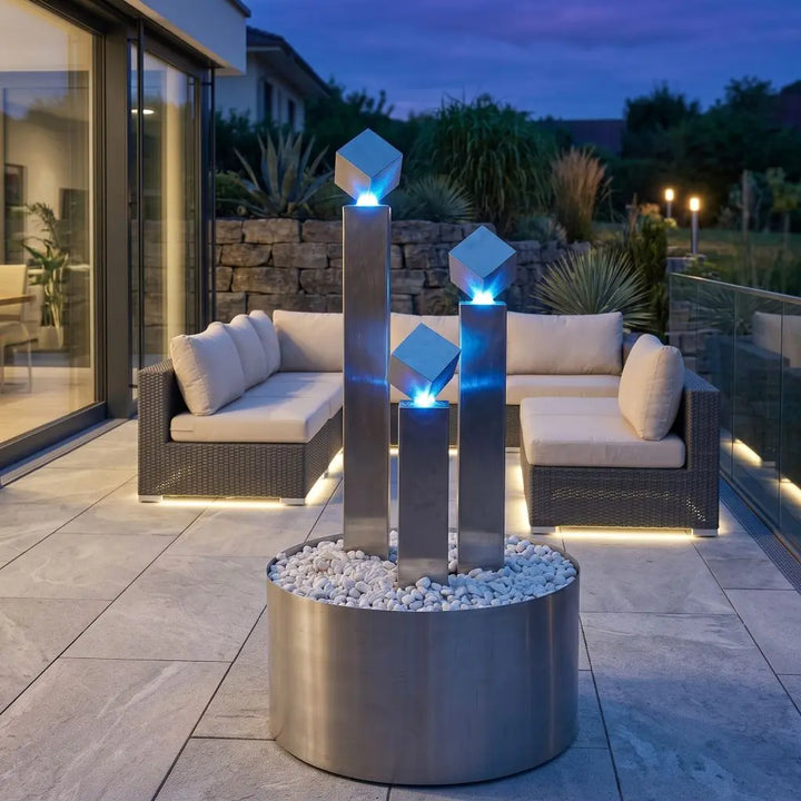 Edelstahl-Gartenbrunnen Balance Cubo 95 cm mit  LED am Wasseraustritt bei
Dämmerung auf Terrasse