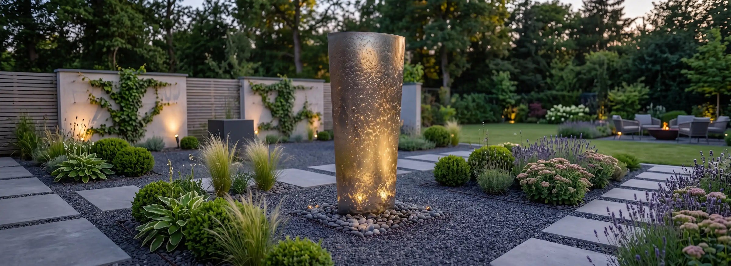 Ellipse Gartenbrunnen aus Edelstahl in einer modernen Gartenanlage bei Nacht beleuchtet